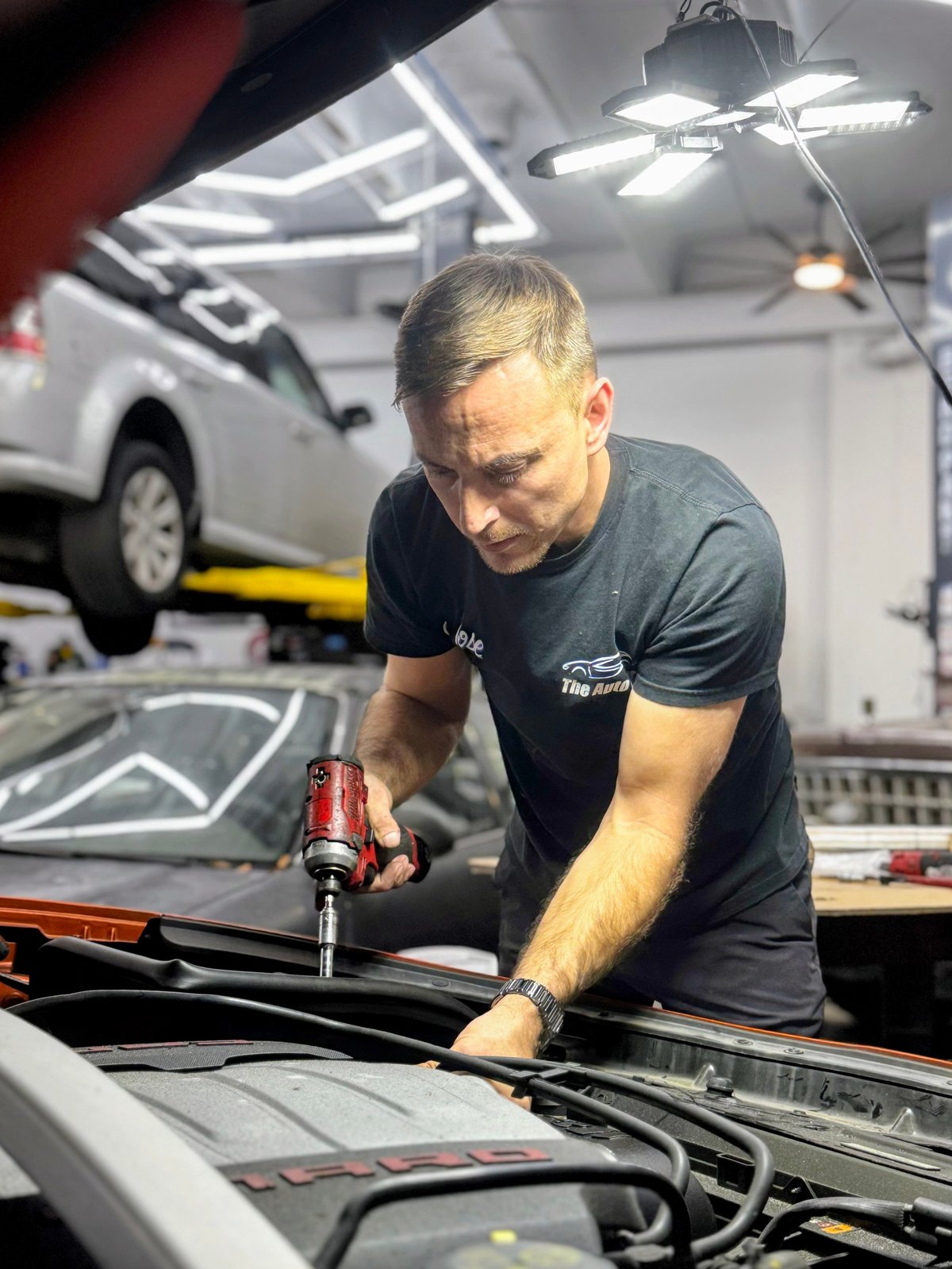 Mechanic working on a car engine in a well-lit garage workshop with vehicles in the background